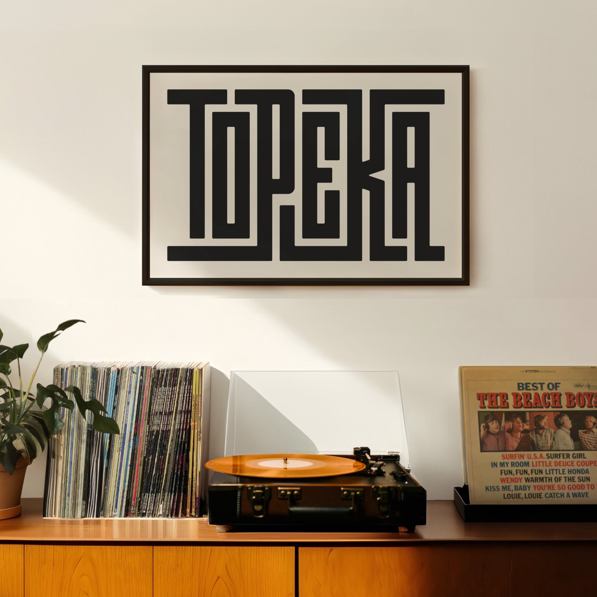Retro Topeka artwork above vintage record player on Mid-Century Modern furniture.